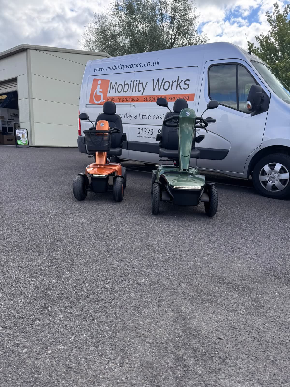 Rear view of the Vermeiren Sync and Kuarz mobility scooters beside the Mobility Works van